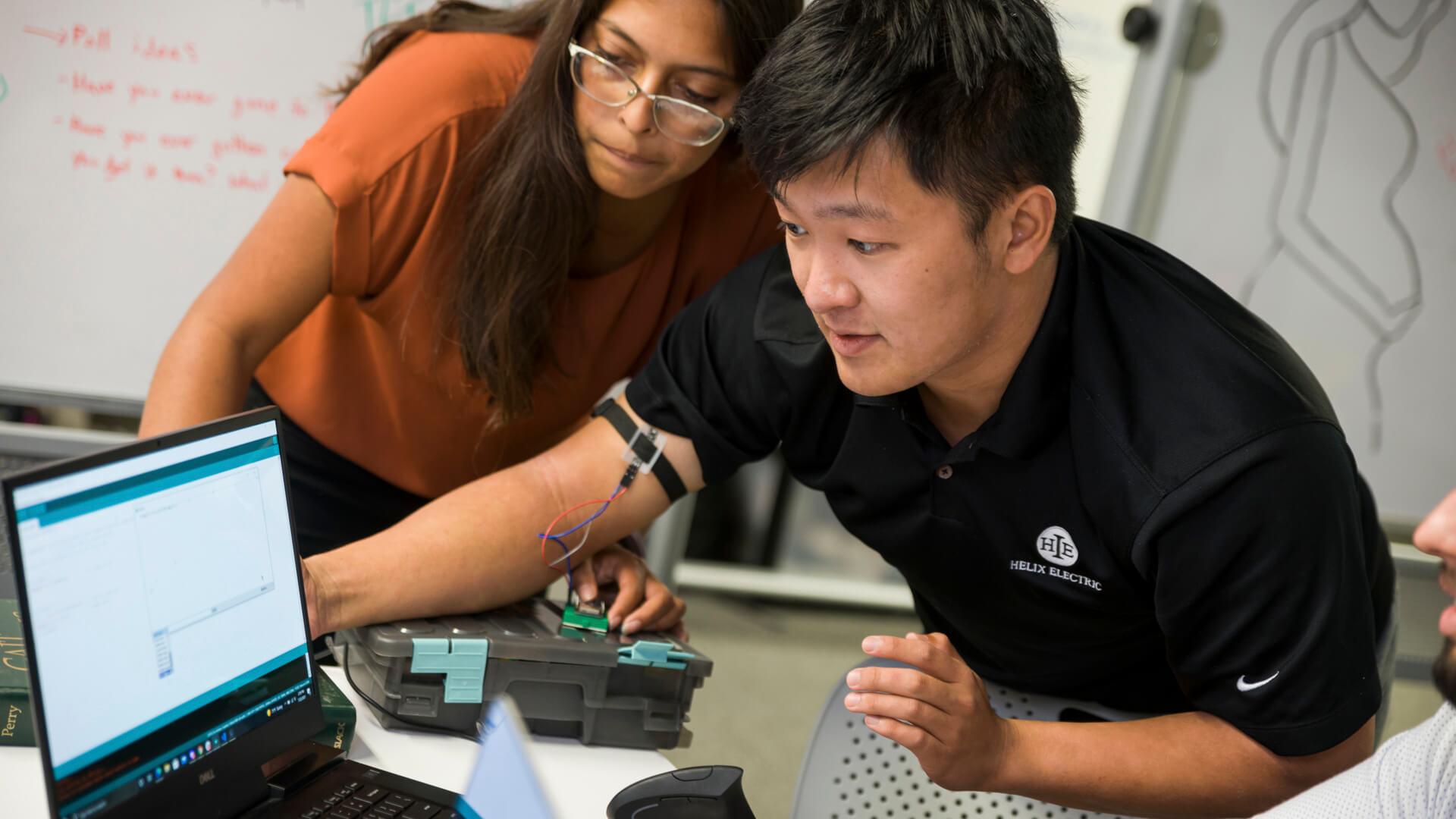 Faculty member and students review a small satellite prototype in a collaborative engineering lab.