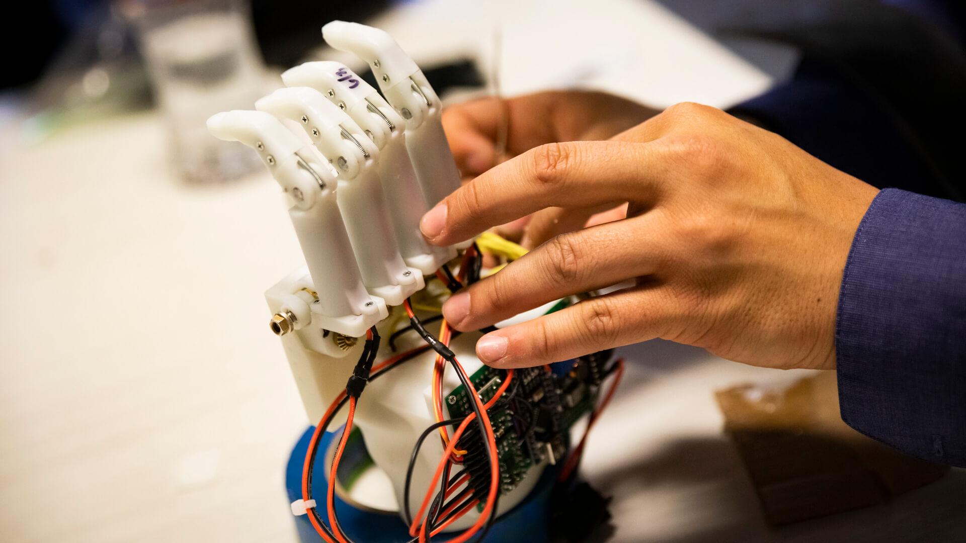 Close-up of a robotic hand prototype being adjusted by a student.
