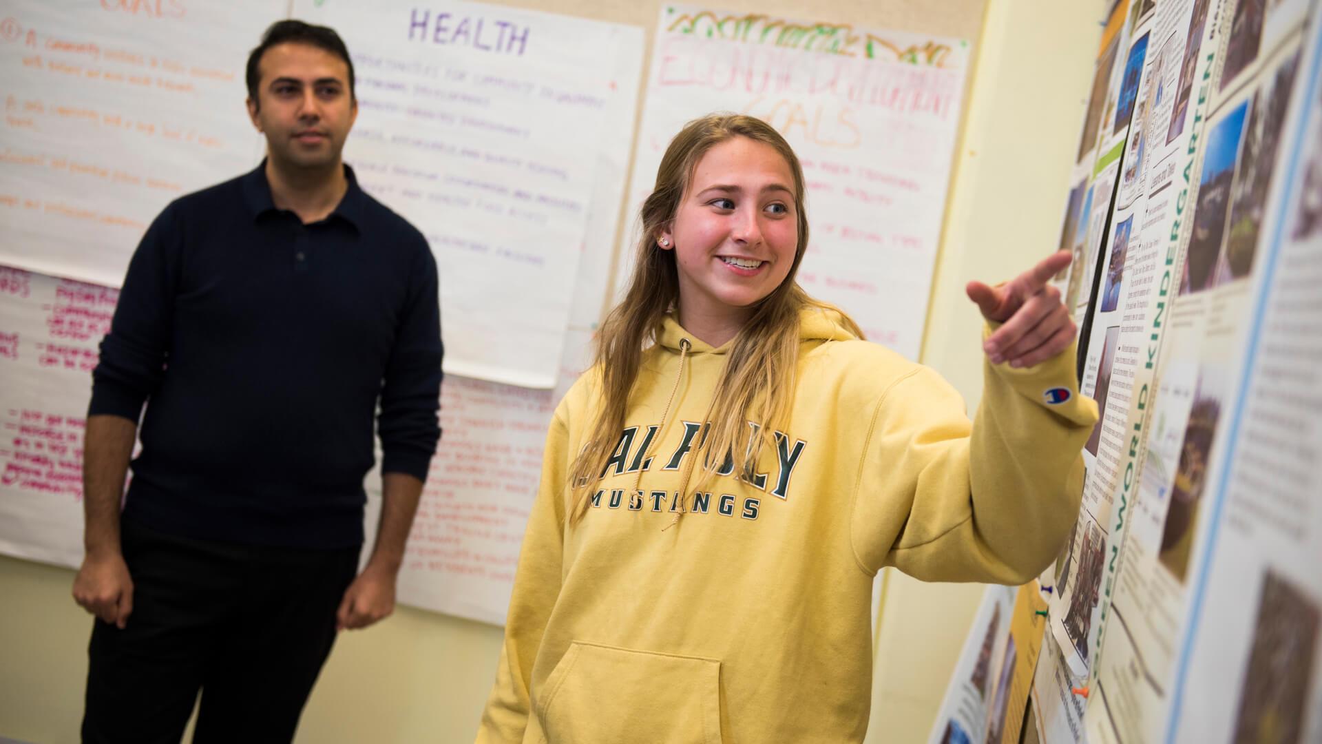 Student presenting research findings on a poster board in a classroom.