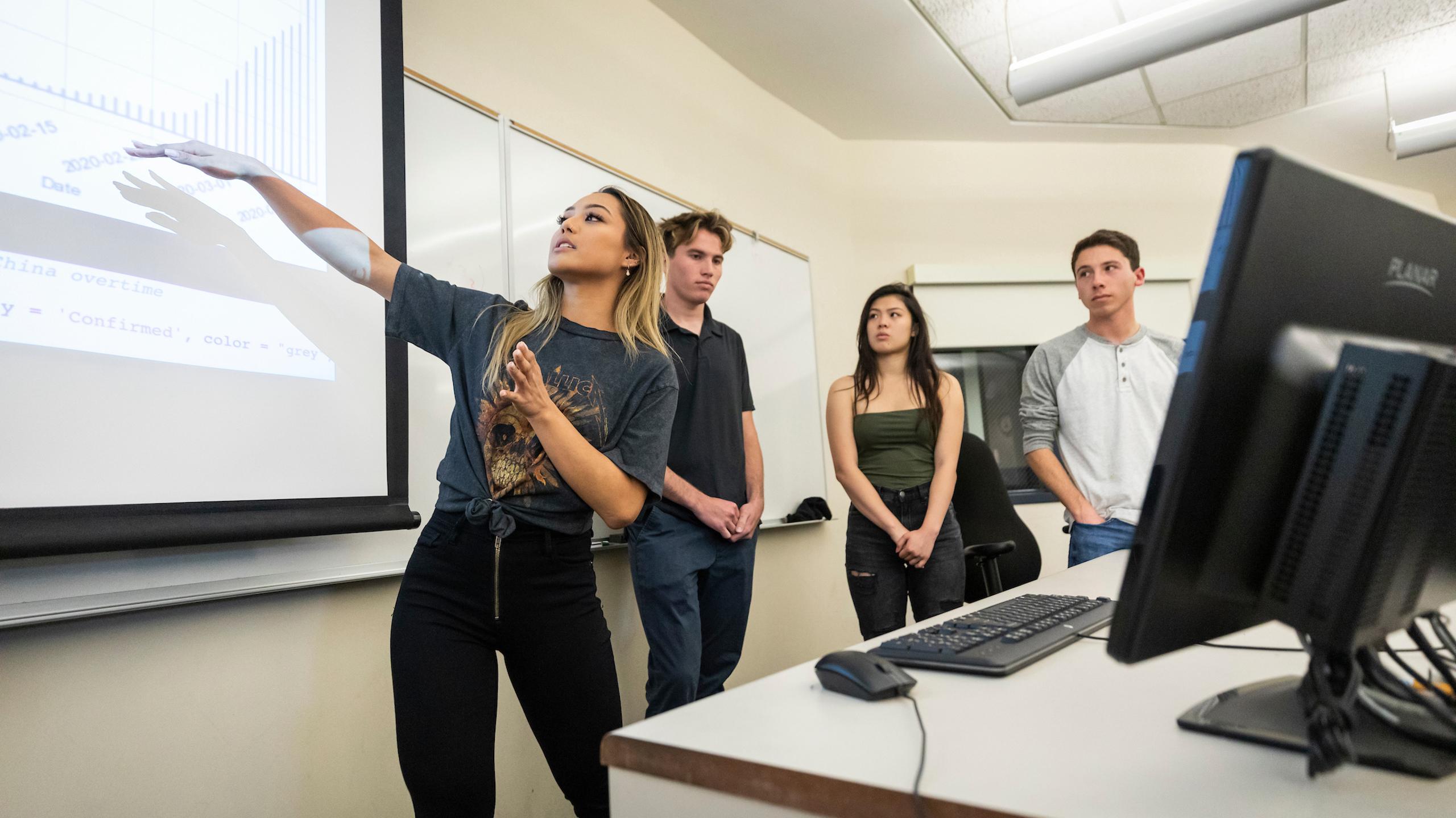 Student presenting statistical data on a projected graph to classmates in a classroom.