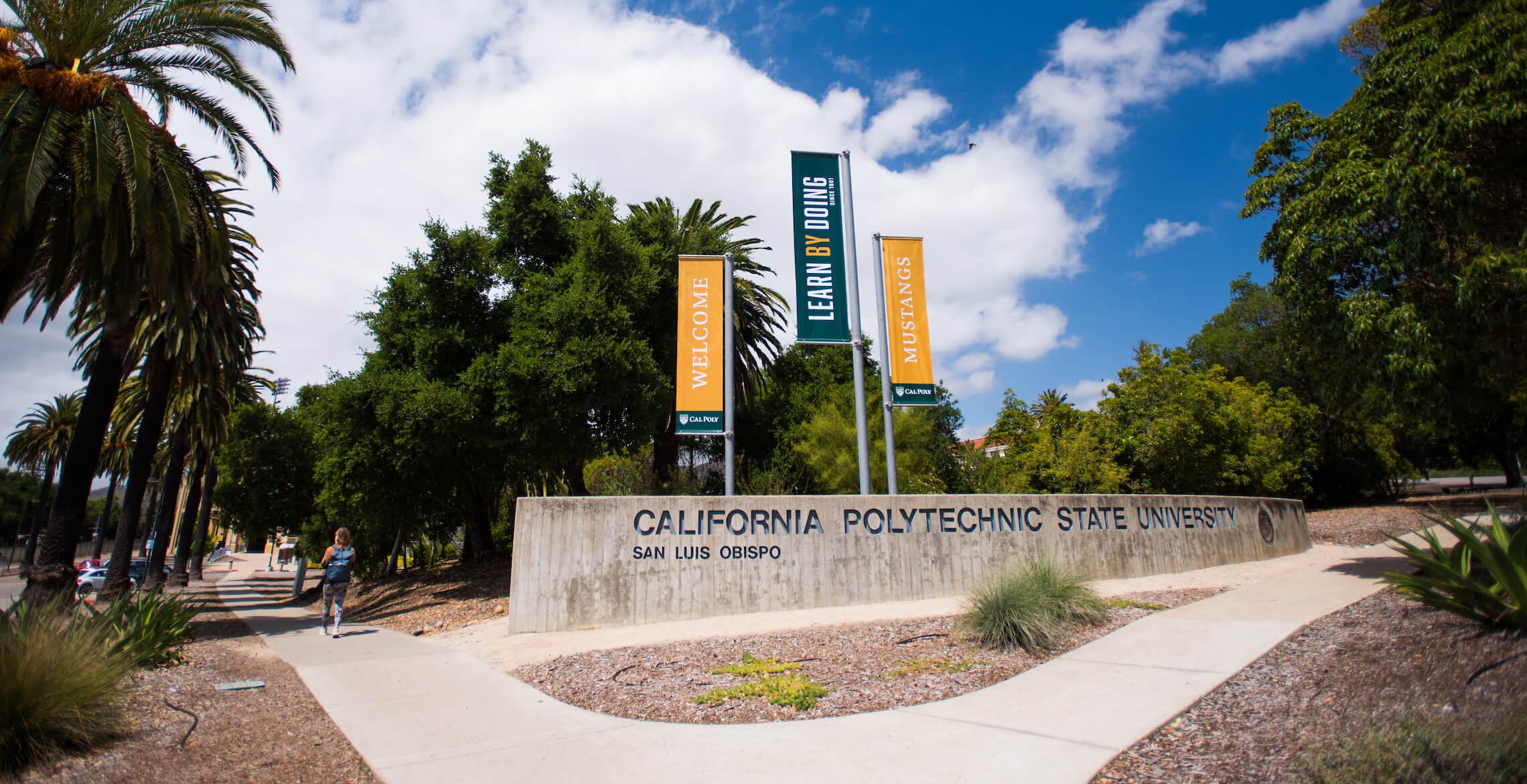 California Polytechnic State University San Luis Obispo sign with banners reading "Welcome," "Learn By Doing," and "Mustangs.