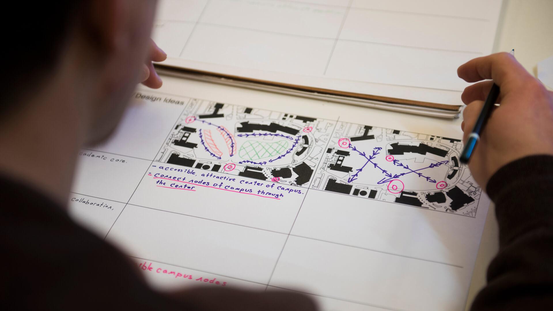 Student reviews a campus site plan with hand-drawn circulation and design notes during a planning studio session.