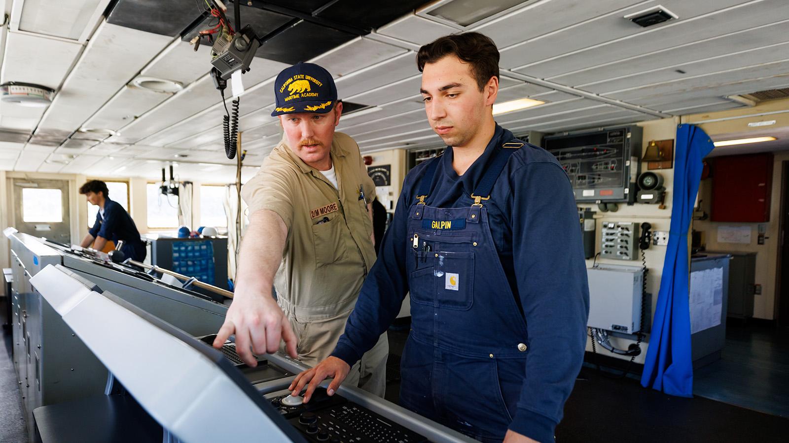 Instructor guiding a student operating navigation and control equipment inside a ship’s bridge.